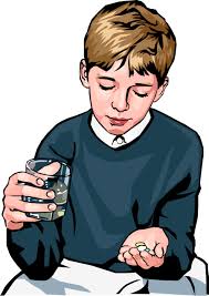 young boy taking medicine with glass of water and tablets in hand 