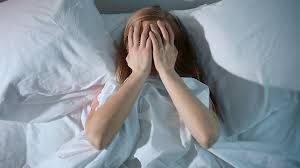 sleeping woman with hands on face in a bed under duvet