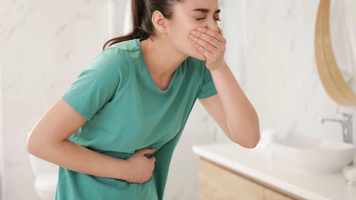 woman in green shirt, hand on mouth and stomach fighting urge to vomit